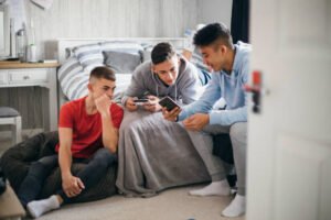 Three teenage boys relaxing and having fun while playing on a games console in a bedroom.