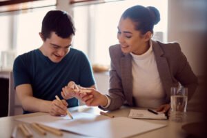 Happy down syndrome man and his psychologist drawing together on the paper during home visit.